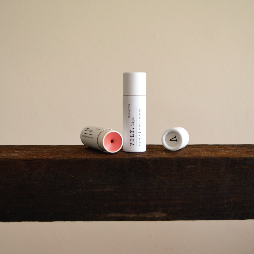 Two lip balm tubes on a wooden shelf with a neutral background