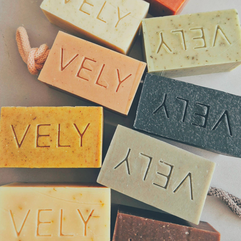 Assorted colored bars of VELY soap on a light background