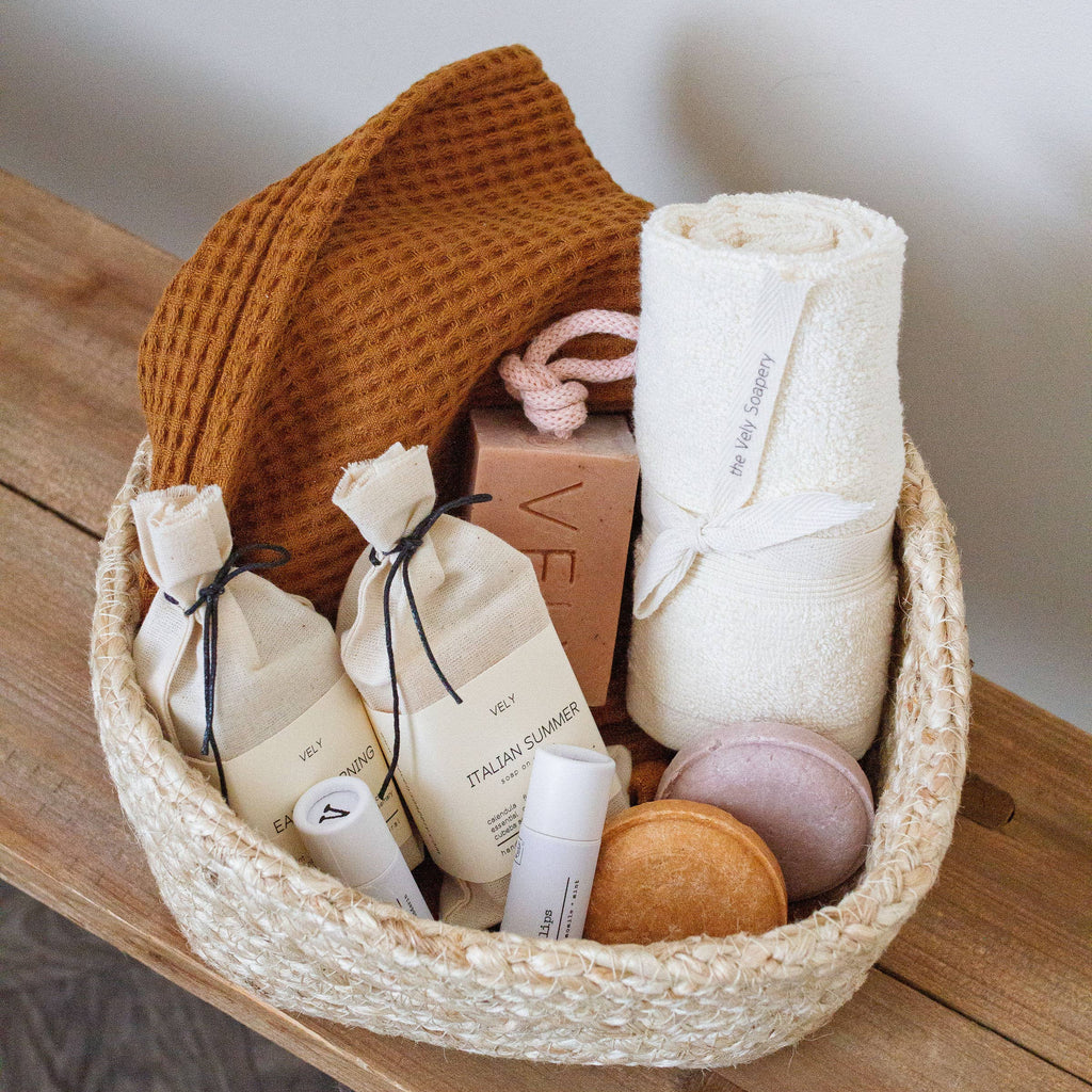 Basket with VELY soap bars in cotton bags brown waffle towel, solid shampoo bars in pink and brown on a wooden surface.