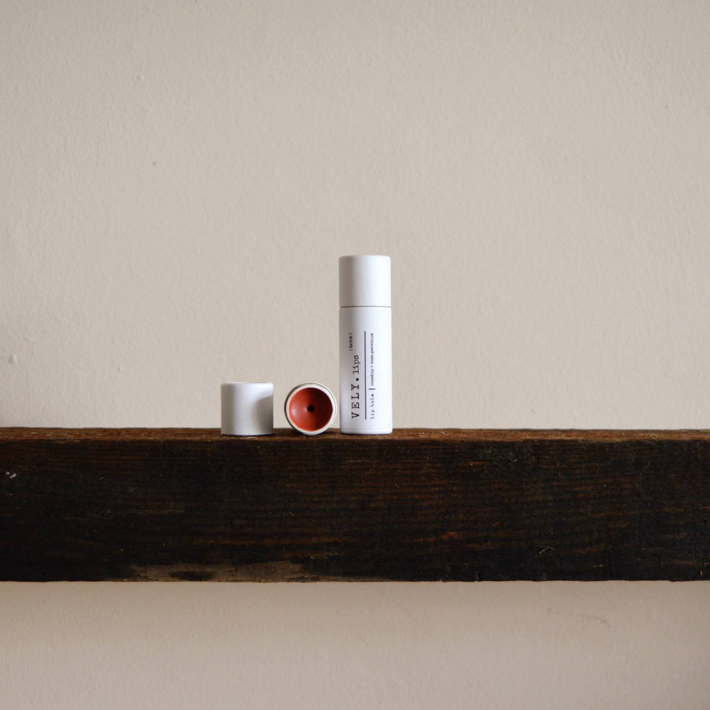 2 tubes of lip balm on a wooden shelf against a plain wall
