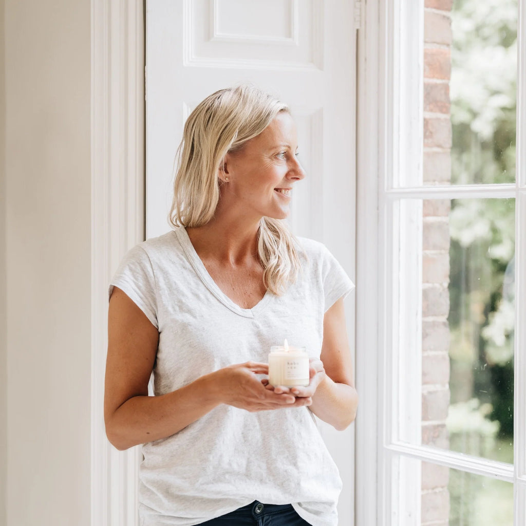Woman holding a candle by a window with a view of greenery