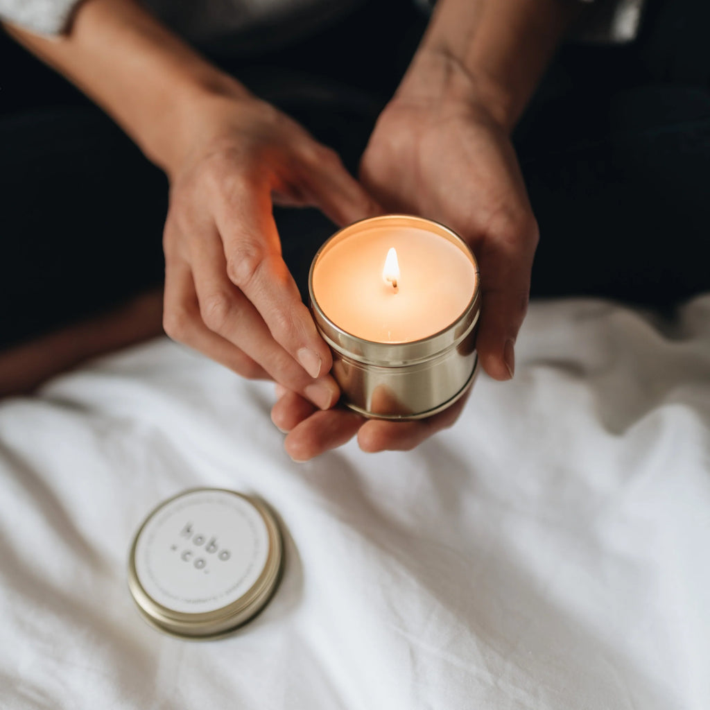 Person holding a lit candle in a tin container on a white surface