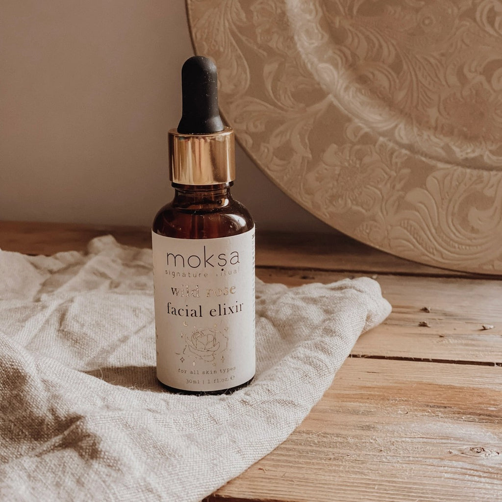 Brown glass dropper bottle labeled 'moksa' on a wooden surface with a textured beige plate in the background.